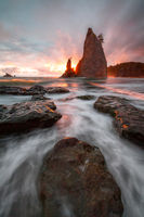 Brilliant sunrays shooting from behind a sea stack on a coastline of the Pacific Northwest.