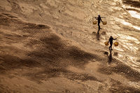 Two women silhouetted on a side-lit mudflat that appears golden.
