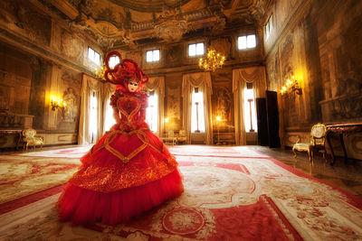 Gorgeous Carnival model wearing an ornate red dress inside a Venetian palace.