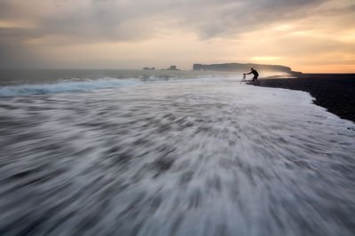 A photographer alone on an Icelandic black sand beach at sunset.