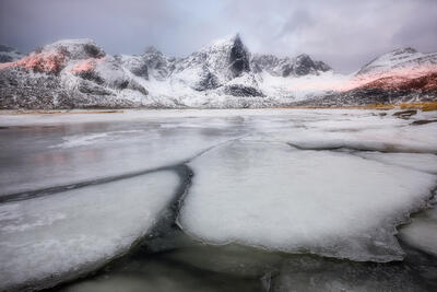 Ice cracks from changing temperatures and melting ice form leading lines to a snow-capped mountain range.