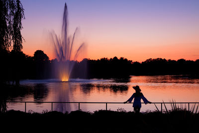 An elegant woman standing in front of a fountain during sunset.