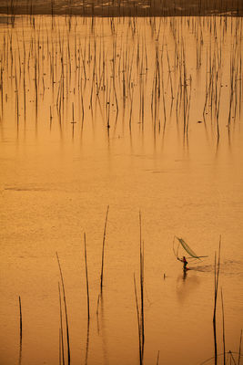 A lone fisherman carrying his net over mud flats at high tide.