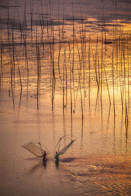 Fishermen holding their nets on a flooded plain during a brilliant sunrise.