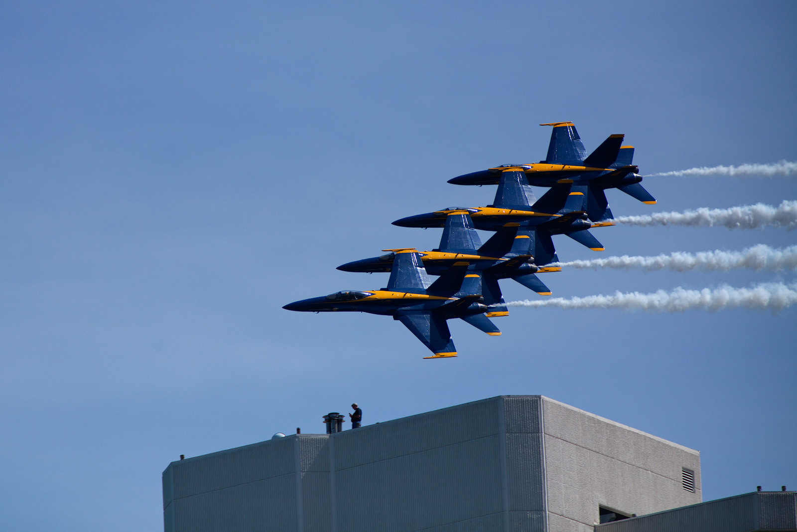 The Blue Angels flying a close pass to a roof worker who is temporarily oblivious to their presence.