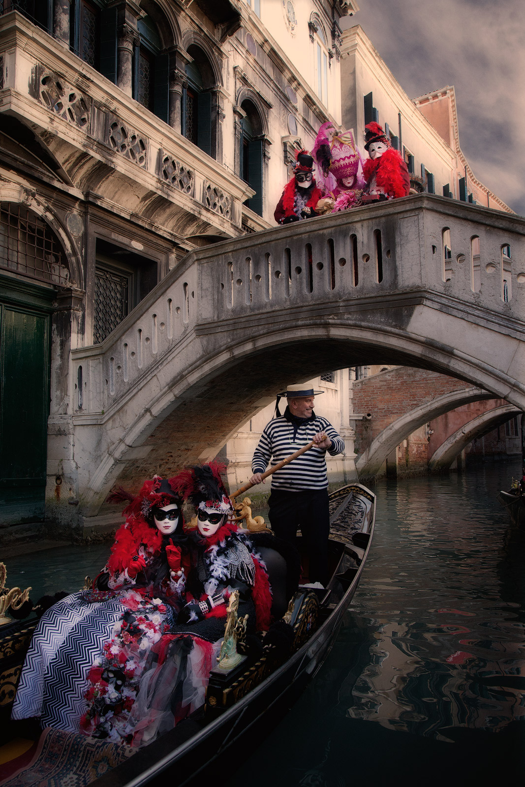 Carnival models riding in a gondola on a Venice canal.