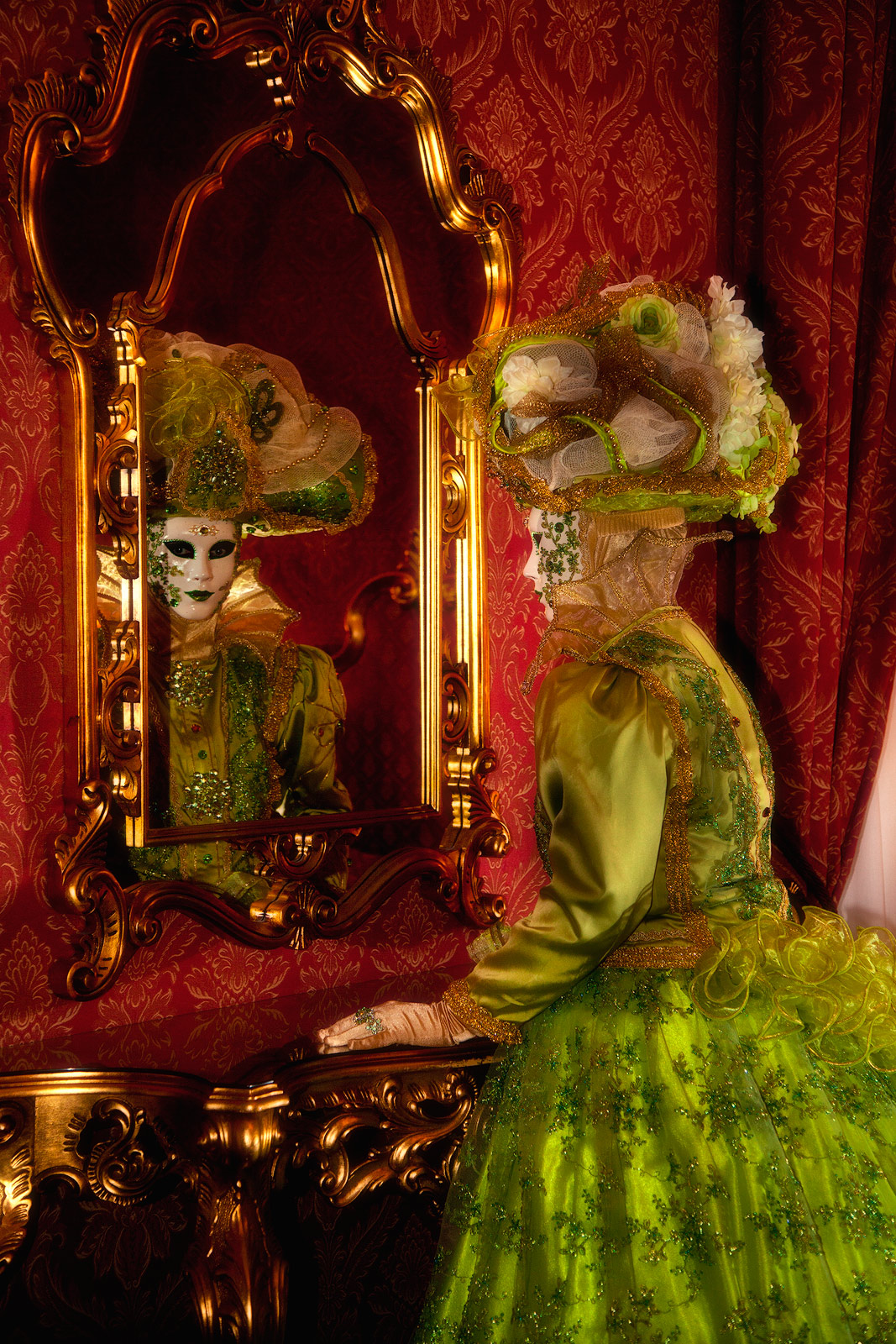 Venice Carnival model gazing into the mirror in an ornate bedroom.