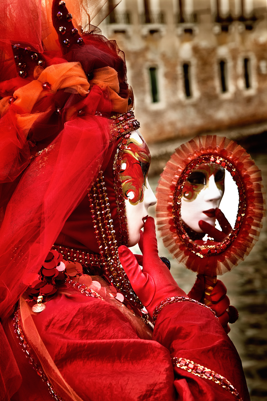 Carnival model in red admiring her mask in a mirror.