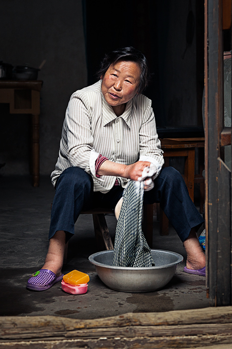 Older Chinese woman reflecting while washing clothes