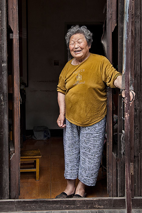Older smiling Chinese woman in the doorway to her home