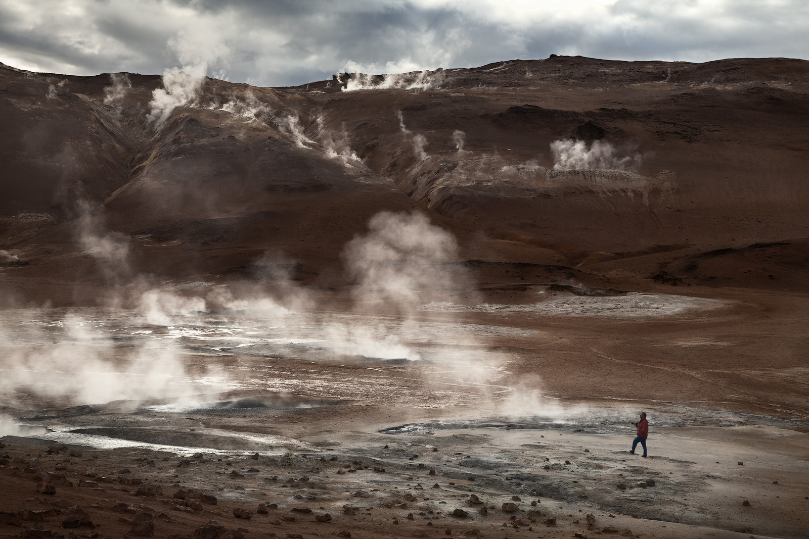 A lone hiker walks through one of Iceland's geothermal fields