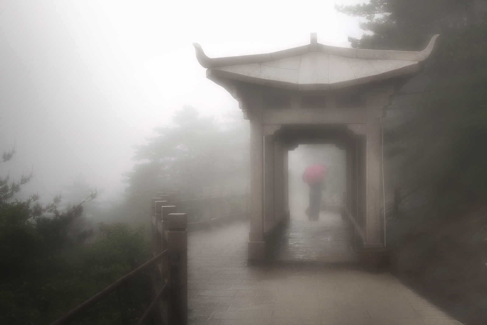 Woman with an umbrella through an archway on a foggy day in China