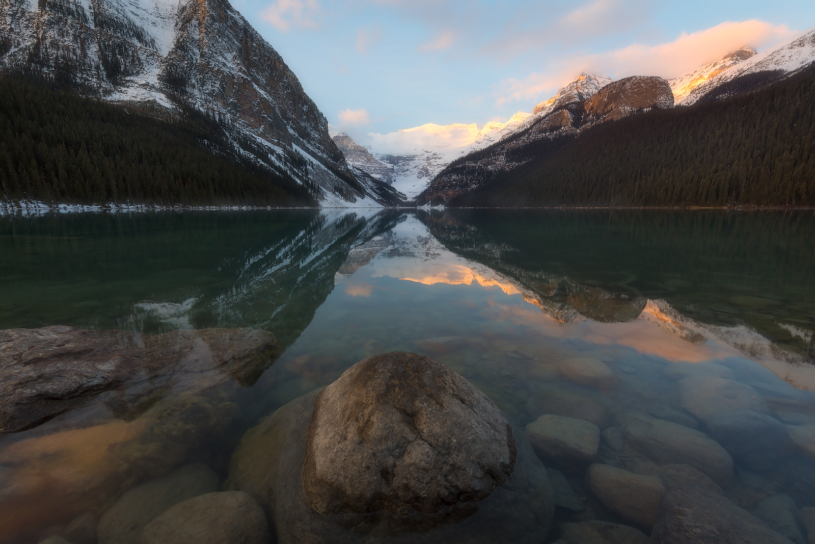 The morning sun peeks over the mountains to light up peaks and clouds over Alberta's Lake Louise.