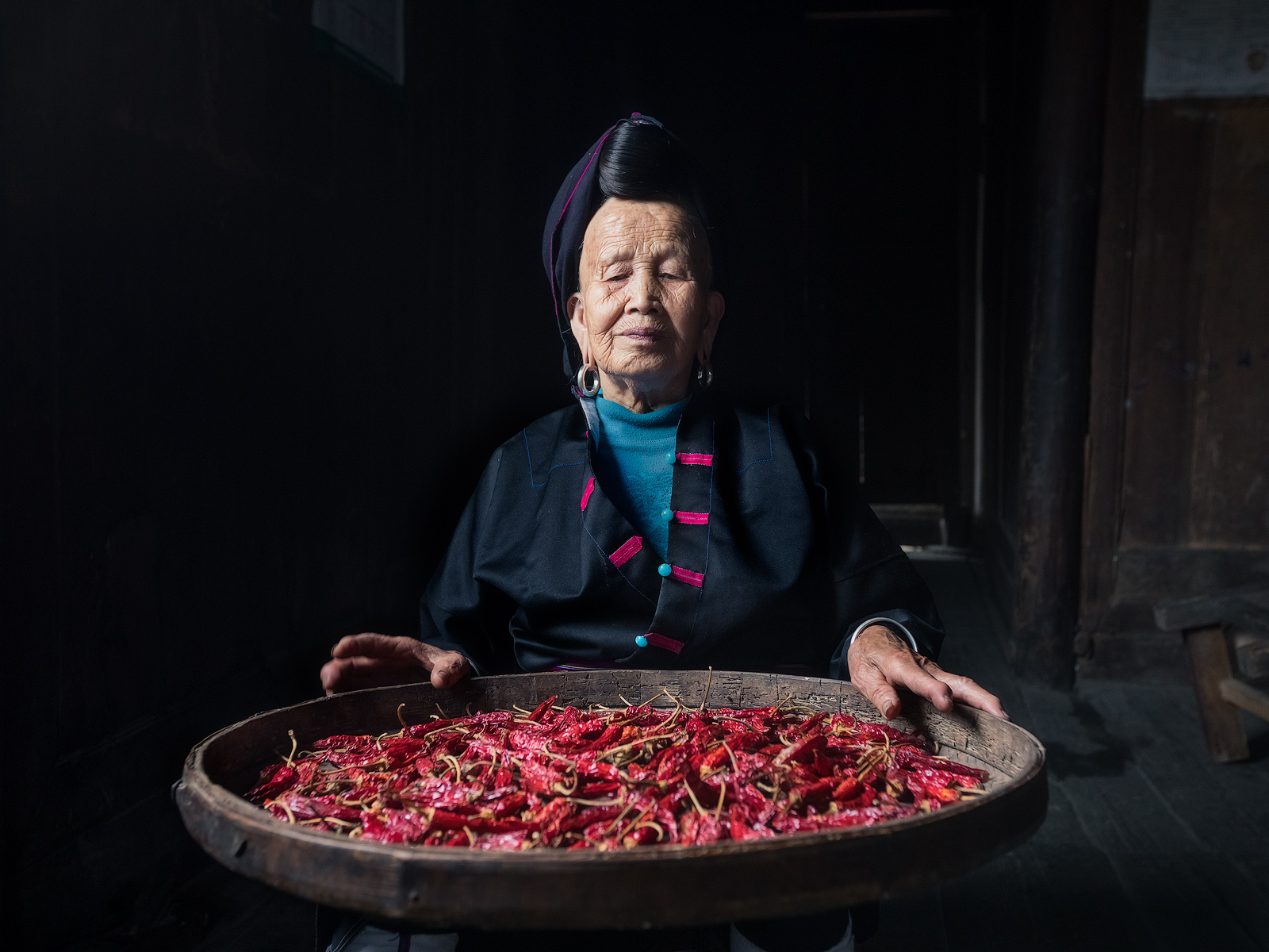 A woman from Da'Zhai rice terraces sorting through chiles in her home.