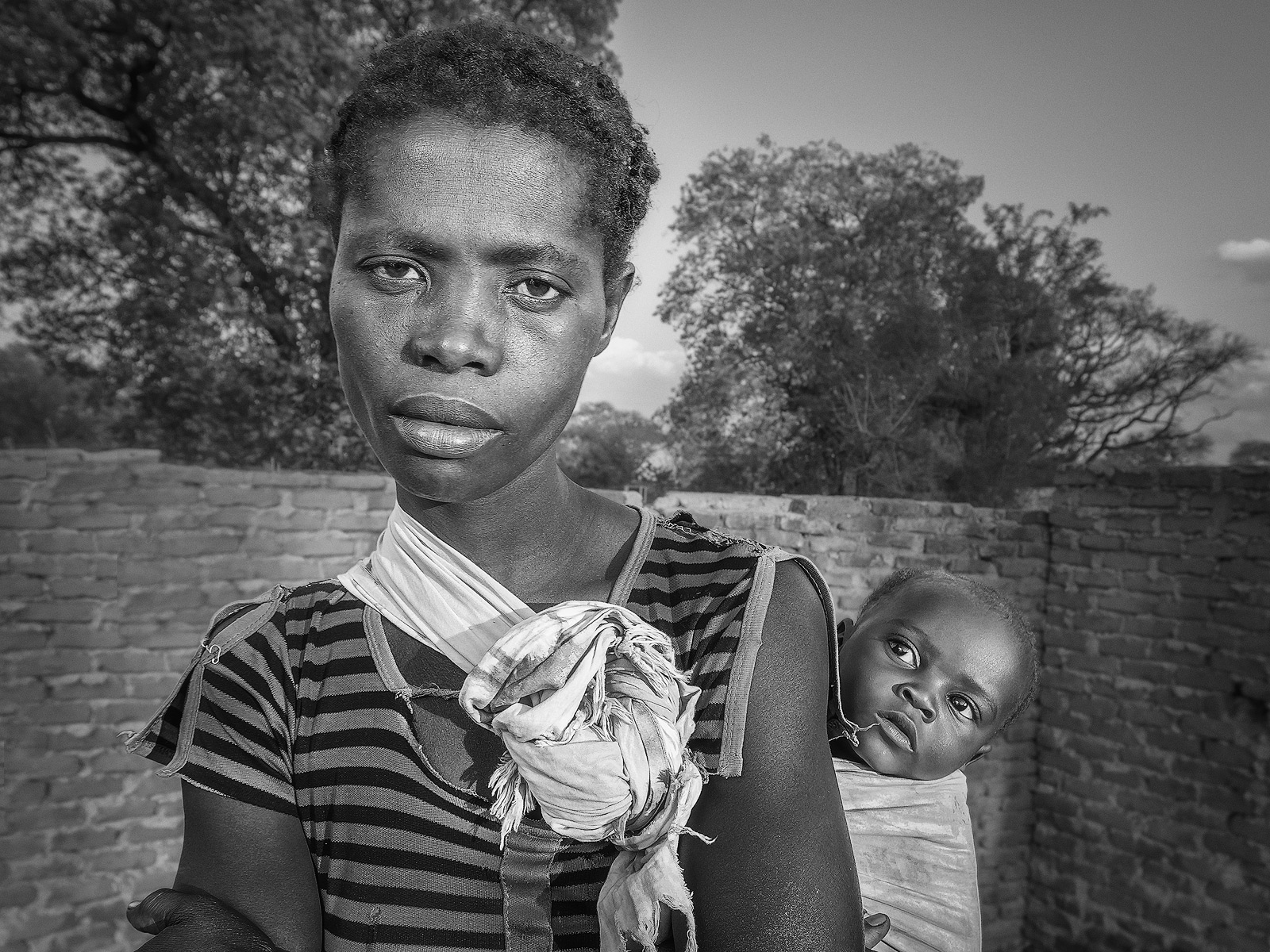 A young Malawian mother carrying her baby in low angled light