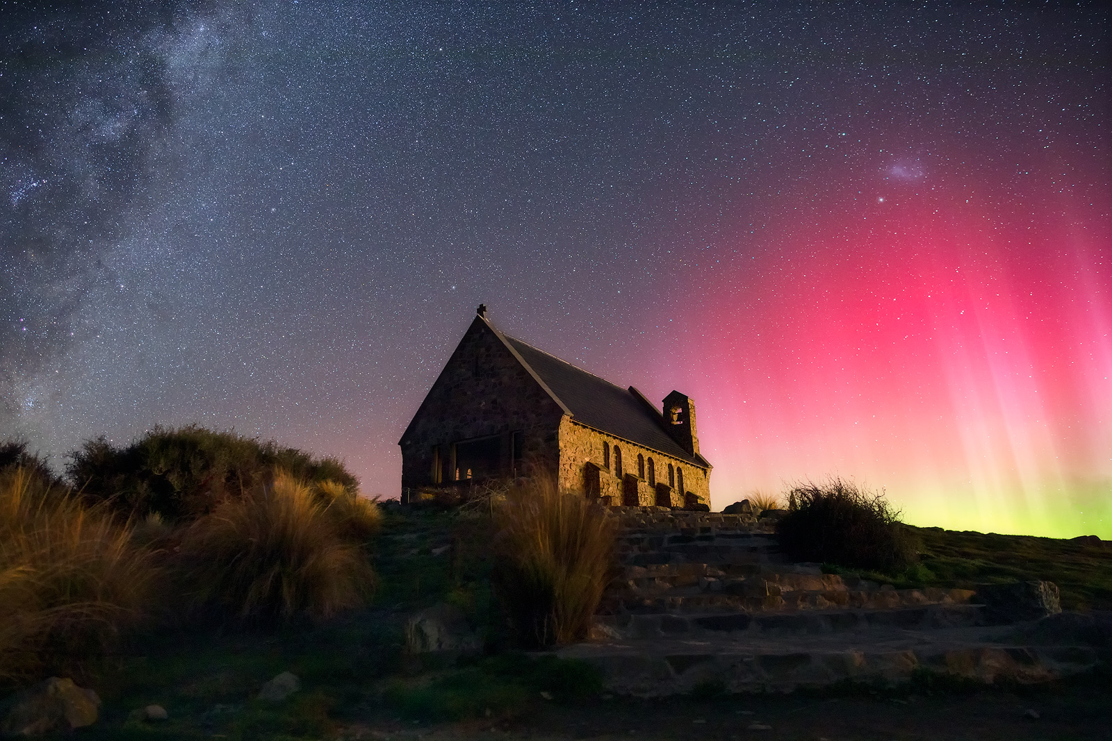 A stone church surrounded by beams from the southern lights (aurora australis) on one side and the Milky Way on the other.