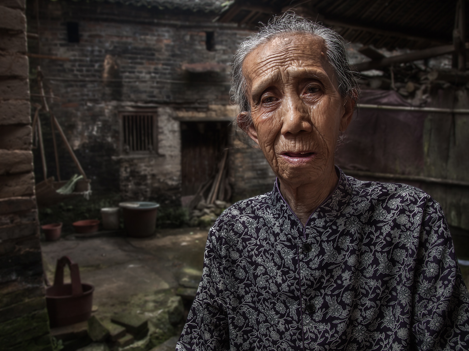 An older, Chinese woman from a small village near XingPing sitting down outside her house.