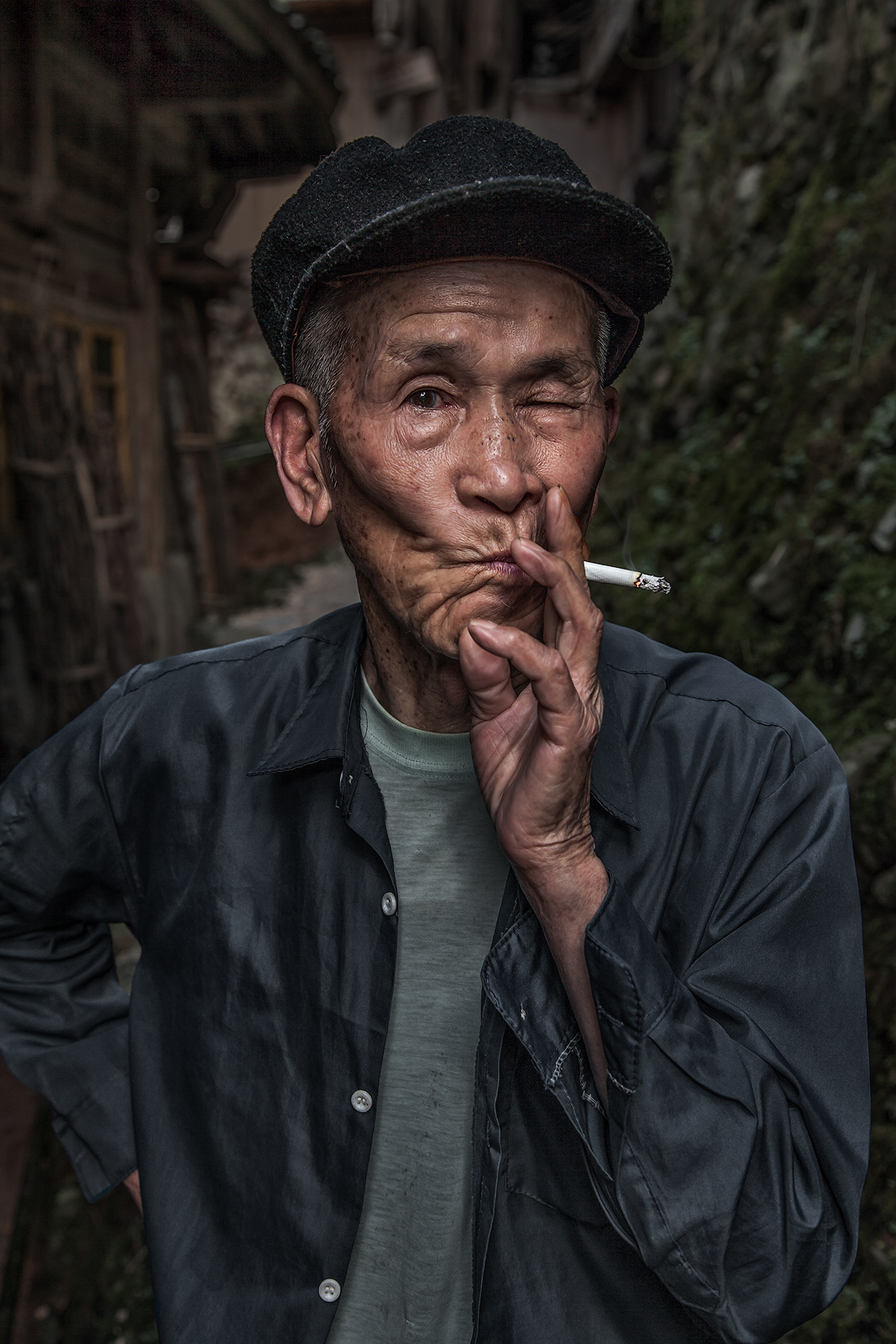 An older Chinese man having a smoke in front of his house.