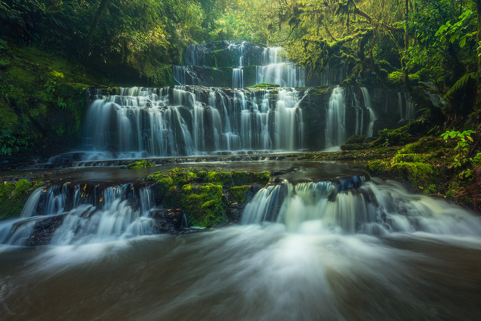 Warm light breaking through tree cover to illuminate a rushing waterfall.