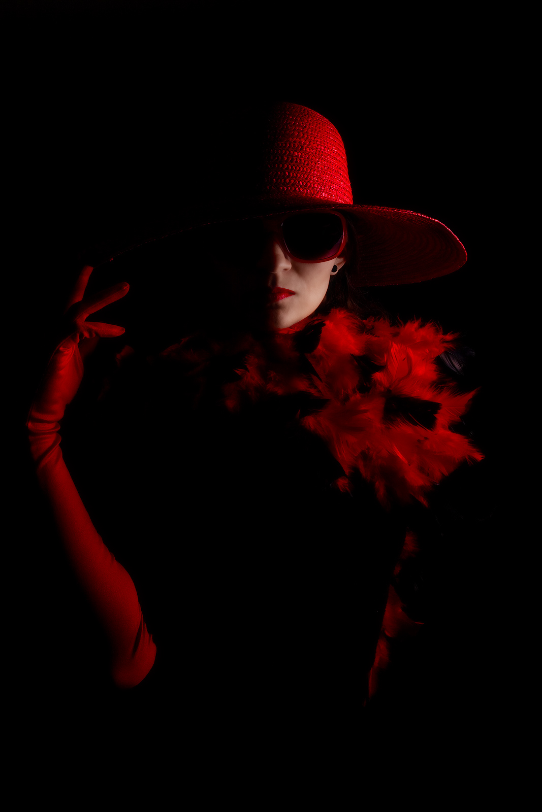 Stylish woman decked out in a red hat and sunglasses against a dark background