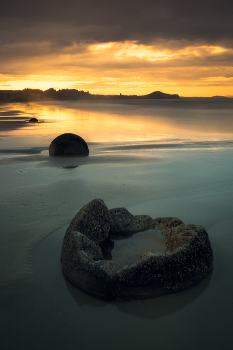 New Zealand's Moeraki Boulders with reflections of sunset behind them.