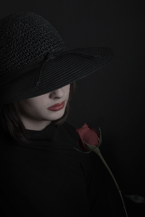 Heartbroken girl wearing black and looking at a red rose