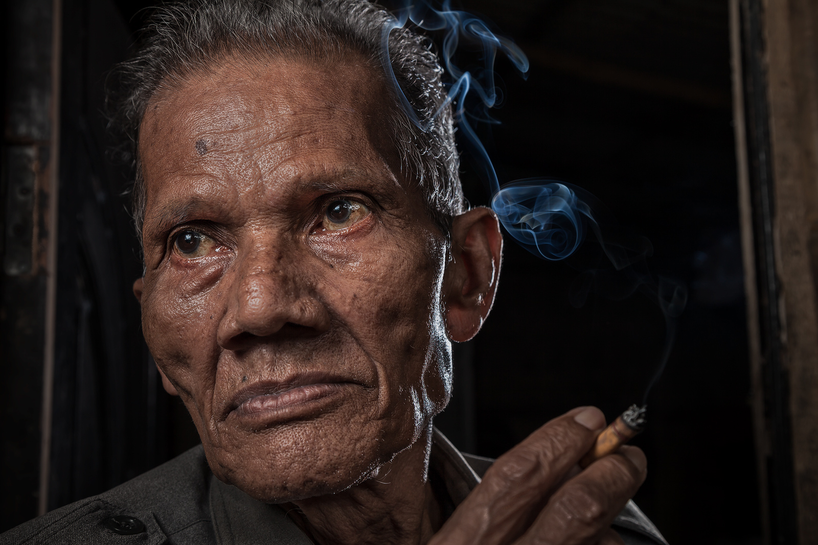 Close-up portrait of Indonesian man smoking in the doorway to his home