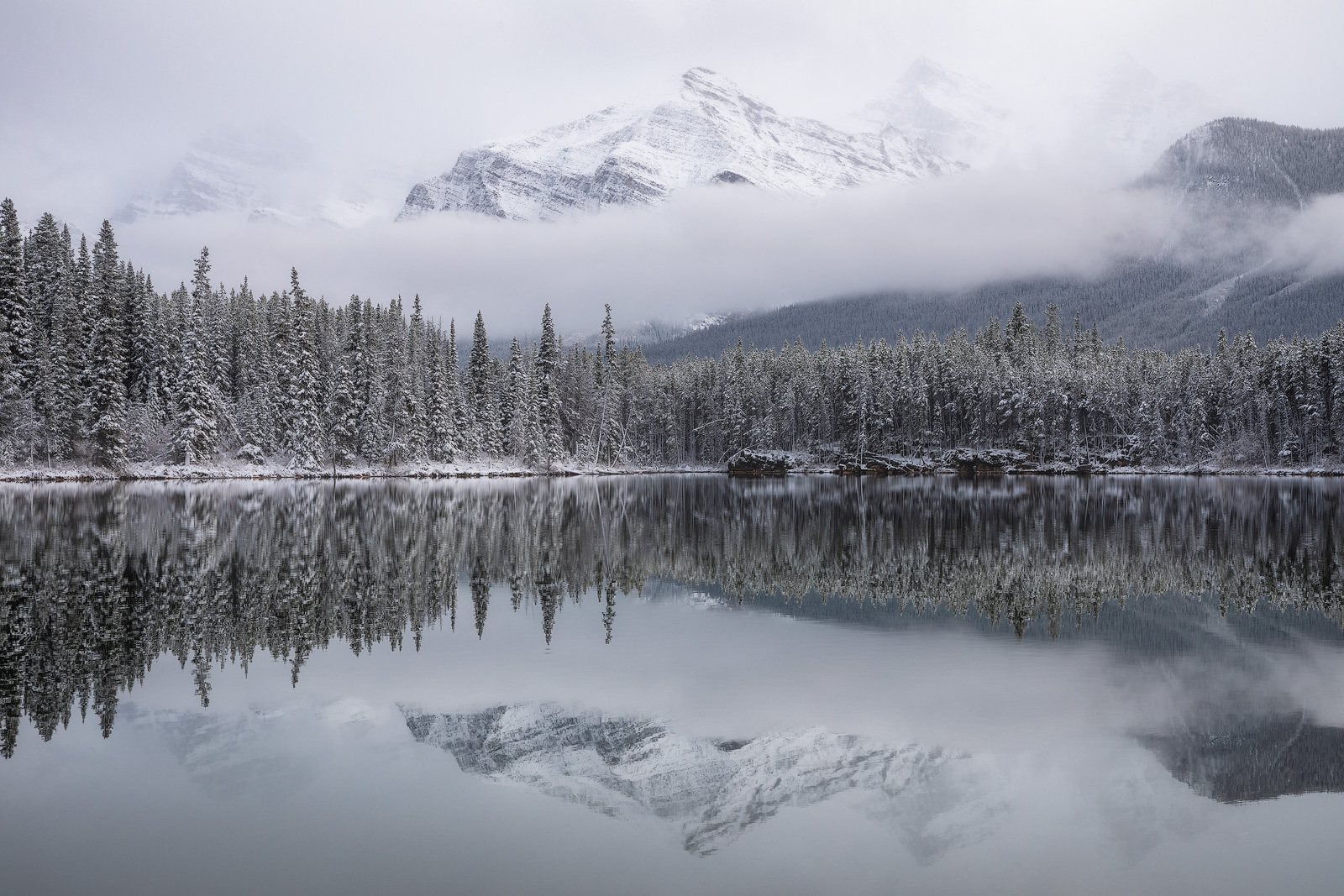 A snow-capped mountain reflected in a lake on a misty morning.
