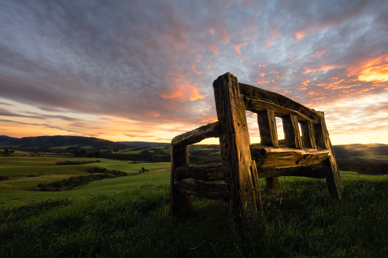 An old wooden bench overlooks a beautiful sunrise over The Caitlins.